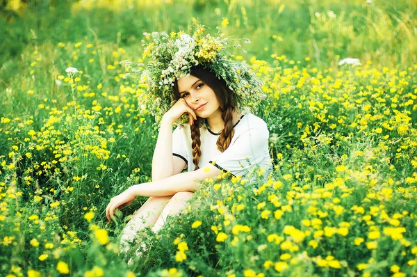 Beautiful girl in wreath of flowers  in meadow on sunny day. Portrait of Young beautiful woman wearing a wreath of wild flowers. Young pagan Slavic girl conduct ceremony on Midsummer.