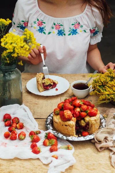 Woman eating a delicious home-made cake with aisheny and stuffed strawberries for dessert. Summer Styled dinner table. Coffee to the cake. sitting at the rustic dining table
