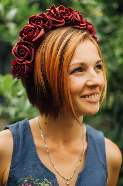 Portrait of a beautiful young woman wearing wreath. Young beautiful woman posing with flowers bouquet on her head. Girl posing in a decorative wreath of artificial flowers on outdoor in the summer