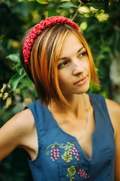 Portrait of a beautiful young woman wearing wreath. Young beautiful woman posing with flowers bouquet on her head. Girl posing in a decorative wreath of artificial flowers on outdoor in the summer