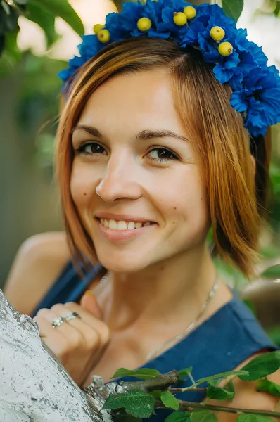 Portrait of a beautiful young woman wearing wreath. Young beautiful woman posing with flowers bouquet on her head. Girl posing in a decorative wreath of artificial flowers on outdoor in the summer