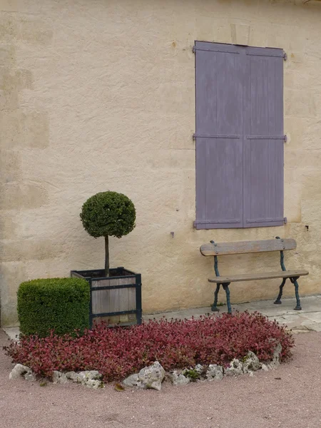 Wooden bench, box bushes, painted shutters and bed of pink plants in Dordogne, France