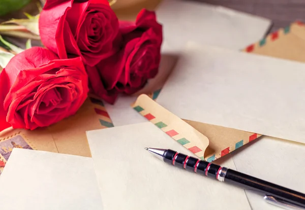 Vintage envelopes, red rose and sheets of paper scattered on the wooden table for writing romantic letters.
