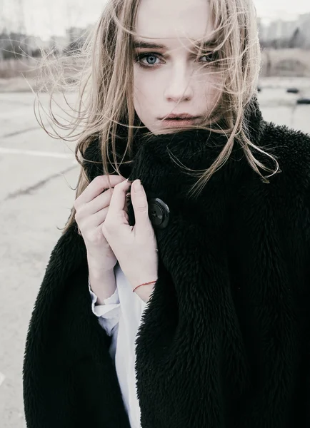 Portrait of a beautiful young blonde woman in a black jacket on the street, cloudy