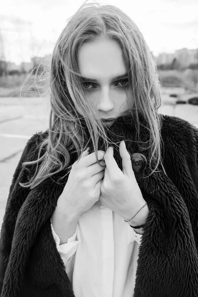 Portrait of a beautiful young blonde woman in a black jacket on the street, cloudy