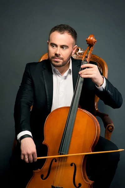 Portrait of young man in black suit sitting on luxury chair with cello