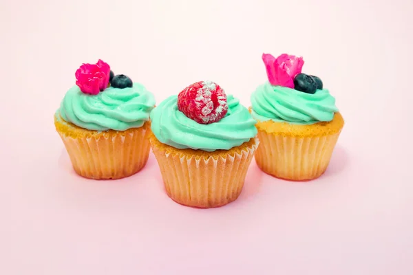 Cupcakes with butter cream and vanilla with raspberry and blueberry with pink flowers on pink background