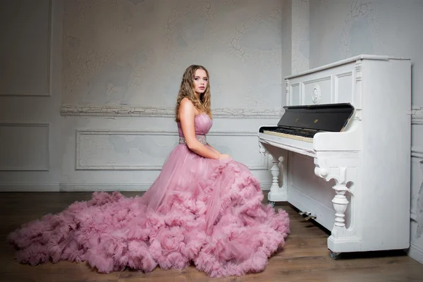 Portrait of young beautiful girl in long pink dress near the piano