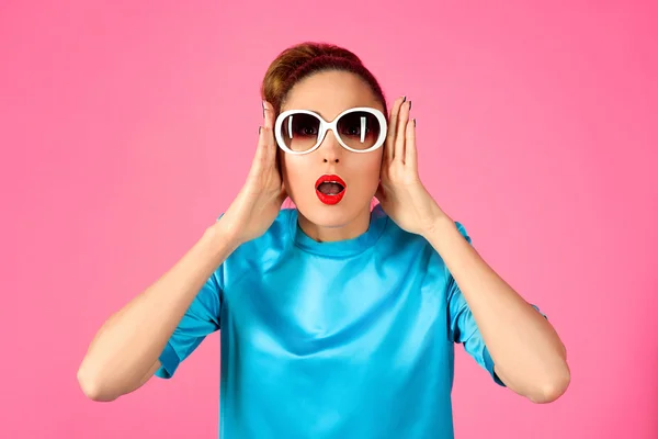 Portrait of young beautiful woman in blue silk dress and white sunglasses ot the pink background