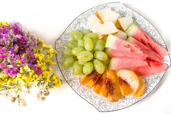 Peach, white grape, watermelon, melon on the plate and dried flowers on white background