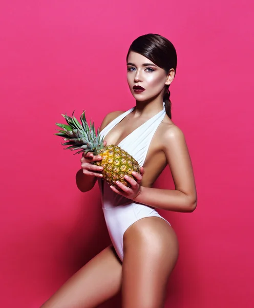 Beautiful sexy young girl standing on a pink background with  magazine  cover with perfect body with bronze tanned skin holding a pineapple  cocktail smiles a lovely smile perfect photos for advertising
