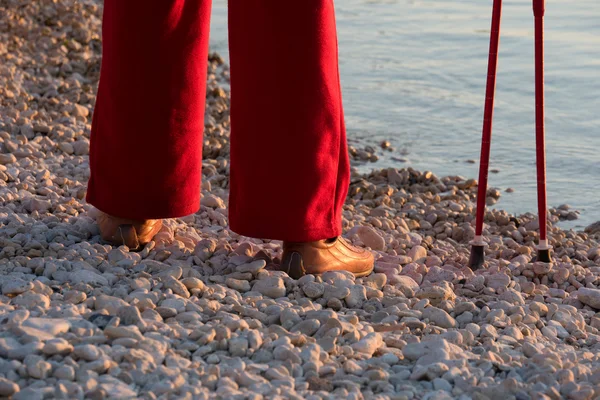 Human legs in red pants with Nordic walking poles in background of sea