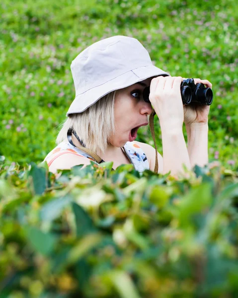 Girl watching someone through binoculars from behind bushes