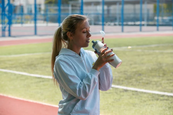Young beautiful sportswoman resting after training. Woman drinking water