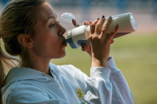 Young beautiful sportswoman resting after training. Woman drinking water