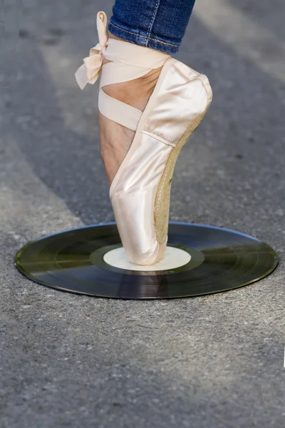 Foot girls in Ballet shoes stands on a vinyl disk.