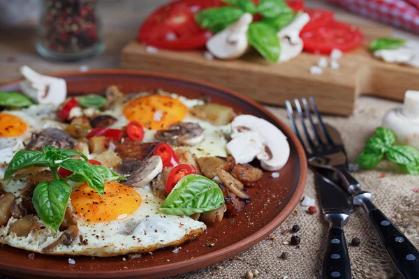 Fried eggs with mushrooms, tomatoes and basil on rustic wooden t