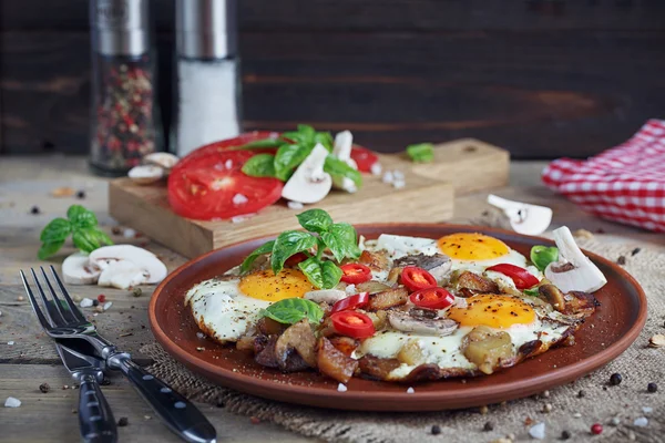 Fried eggs with mushrooms, tomatoes and basil on rustic wooden t