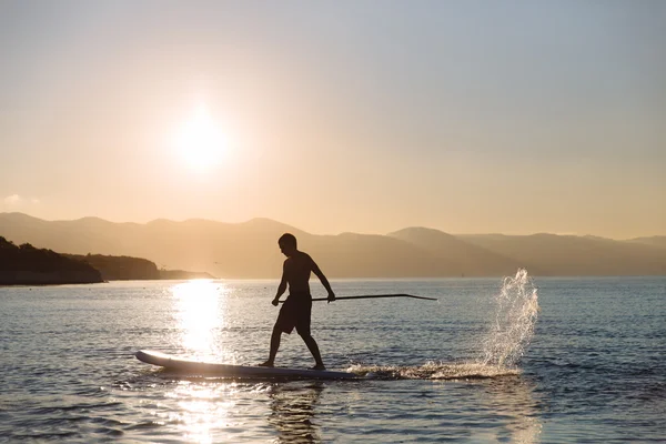 Silhouette of young boy paddle boarding at sunset. concept  lifestyle sport