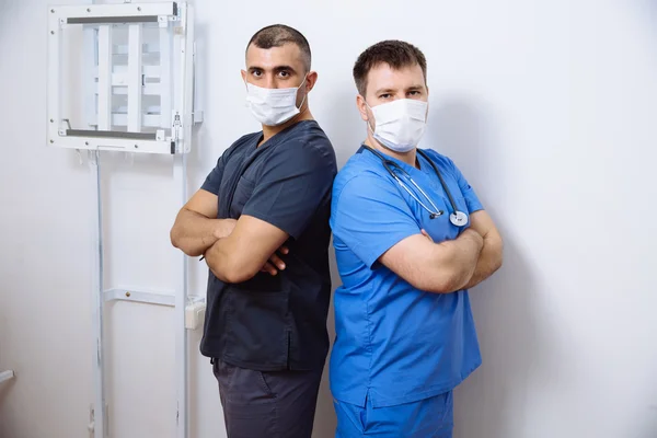 Two surgeons in sterile uniforms standing back to  with arms folded and looking camera on white background
