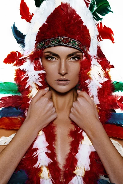 Pretty girl model in a hat with bright feathers in the Indian style on gray background