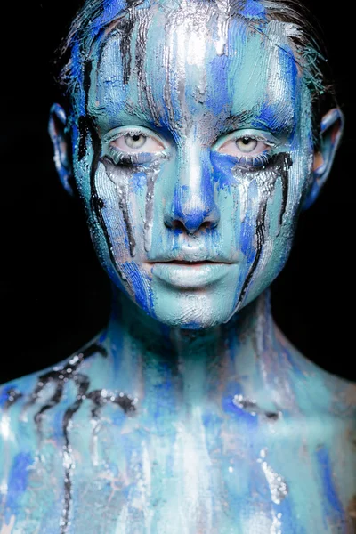 Abstract art makeup. Face, neck and hair girls smeared with bright colors of blue, blue and silver colors. The paint flows. On the face of silver tears. Holi festival