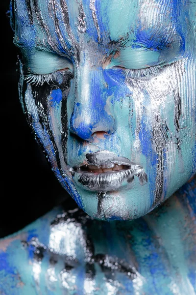Abstract art makeup. Face, neck and hair girls smeared with bright colors of blue, blue and silver colors. The paint flows. On the face of silver tears. Holi festival
