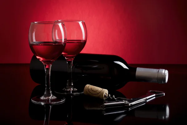 Two glasses with red wine and bottle isolated on red and black background
