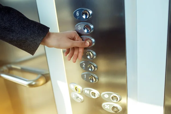 Inger presses the elevator button. Red button.