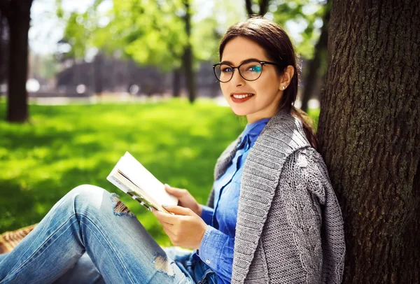 Beautiful relaxed young woman reading a book at the lawn with sun shining.