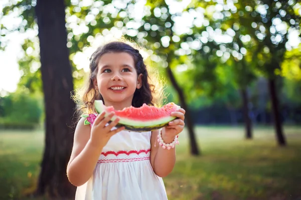 Funny kid eating watermelon outdoors in summer park, focus on eyes. Child, baby, healthy food. Youth lifestyle.