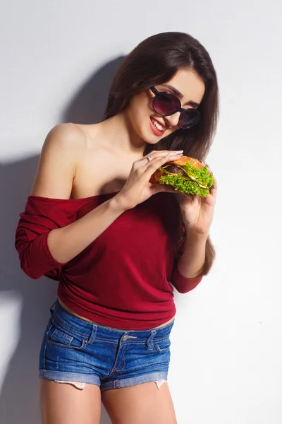 Young beautiful girl with a burger in her hands. Studio shot. Model. Fast food meal