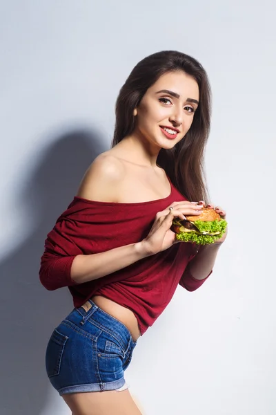 Young beautiful girl with a burger in her hands. Studio shot. Model. Fast food meal