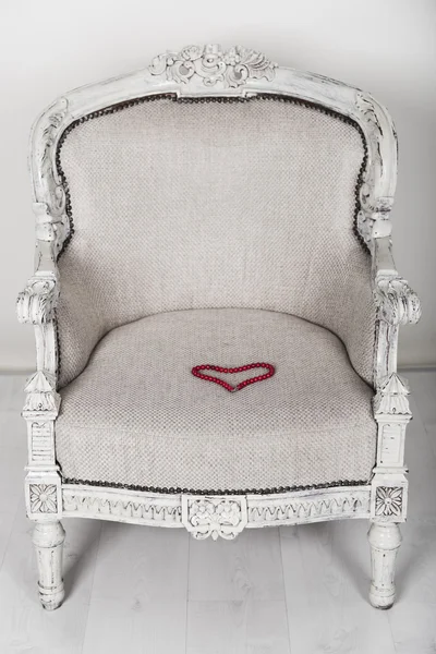 Soft white wooden chair in baroque style and red necklace