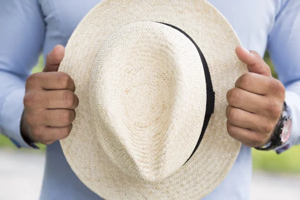 Man in blue shirt holding with hands white wicker hat