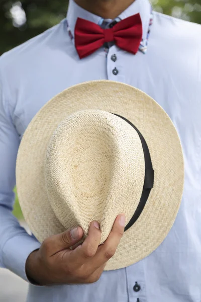 Man in shirt, red bow-tie holding white wicker hat