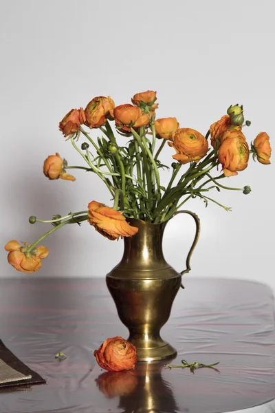 Old vase with orange flowers on the table.