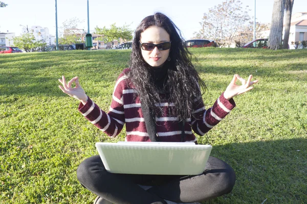 Woman doing yoga in a park with her computer