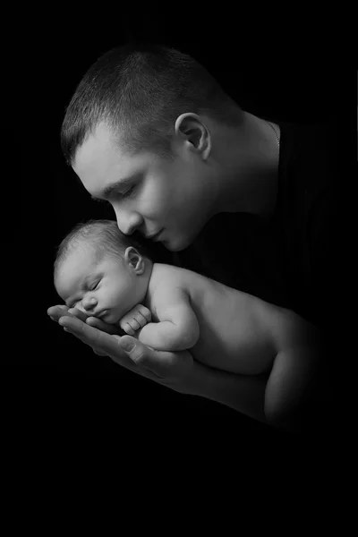 Happy family , young parents holding a newborn baby in her arms and gently hugged him, black and white photo on a black background .