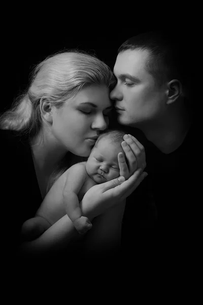 Happy family , young parents holding a newborn baby in her arms and gently hugged him, black and white photo on a black background .