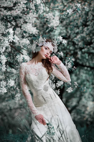 Beauty woman bride in her wedding dress and decoration in her hair in a lush garden of apples .