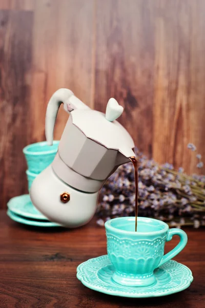 Levitation coffee. Percolator coffee with the lid closed. Pastel blue coffee maker pouring coffee into a cup. Dry lavender behind. Dark wood background