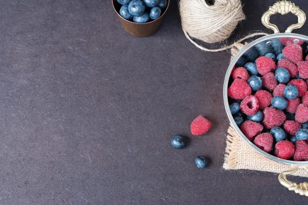 Fresh raspberries and blueberries dark picture with copy space on left. Fresh fruits, berries in an old copper cup, bowl. Dark Styled Stock Photo, Black Background