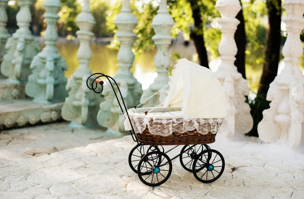 Doll\'s pram. Vintage doll stroller placed on the stairs to a beautiful lake. Retro cart dolls made of rattan and white lace.