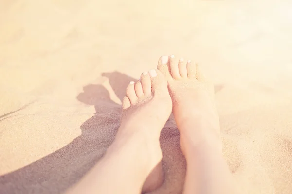 Holiday concept. Woman feet close-up relaxing on beach, enjoying sun and splendid view. Sandy feet on the beach. Sun, sun haze, glare