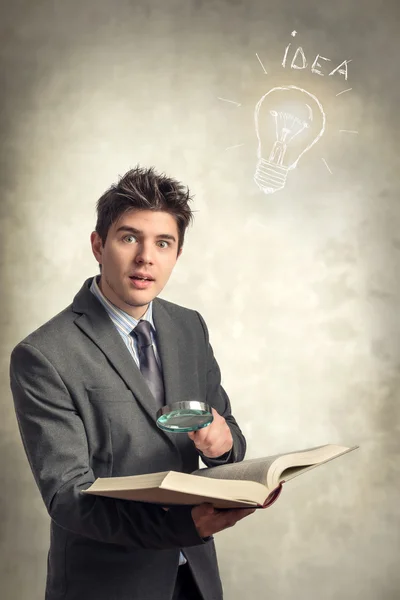 Young businessman looking at a book with magnifying glass
