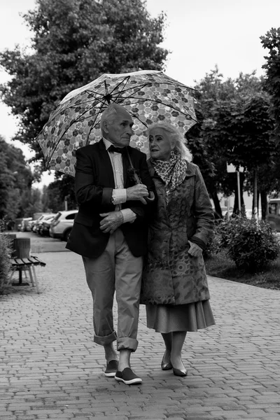Elderly couple walking under an umbrella in the rain. Black and