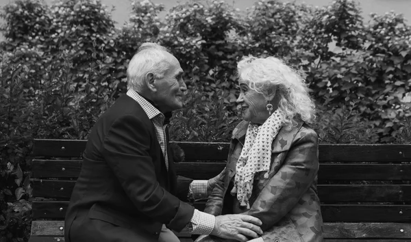 Elderly man and  woman sitting on a bench talking. Black and whi