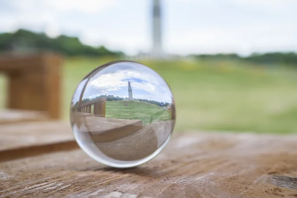 Travel concept. The cozy wooden table with a glass ball. Reflection on the ball is the mother monument patron in Cheboksary, Chuvash Republic, Russia. 06/23/2016