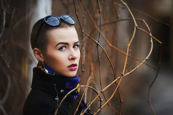 Short-haired woman in a black coat looking seriously among sprigs of spring